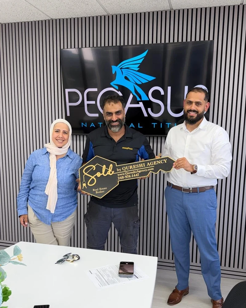Happy home buyers holding Sold key sign with broker Sam Qureshi at Pegasus National Title closing room in Southeast Michigan